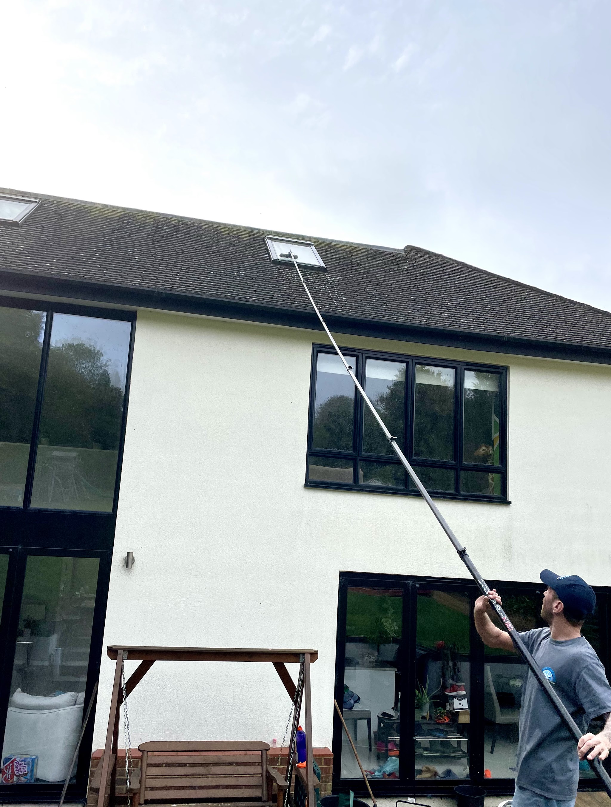 Our window cleaner in a Roundhouse cap and T-shirt, guiding a long pole up a white rendered house