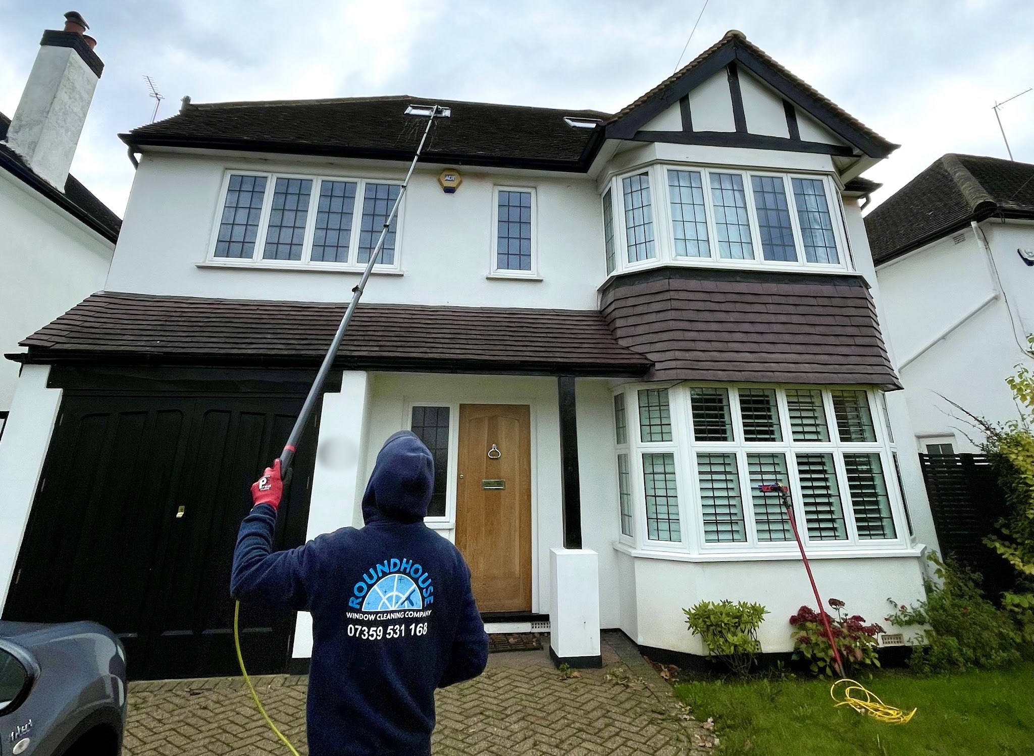 Our window cleaner in a navy Roundhouse hoodie, cleaning the upstairs windows of a white house with bay windows