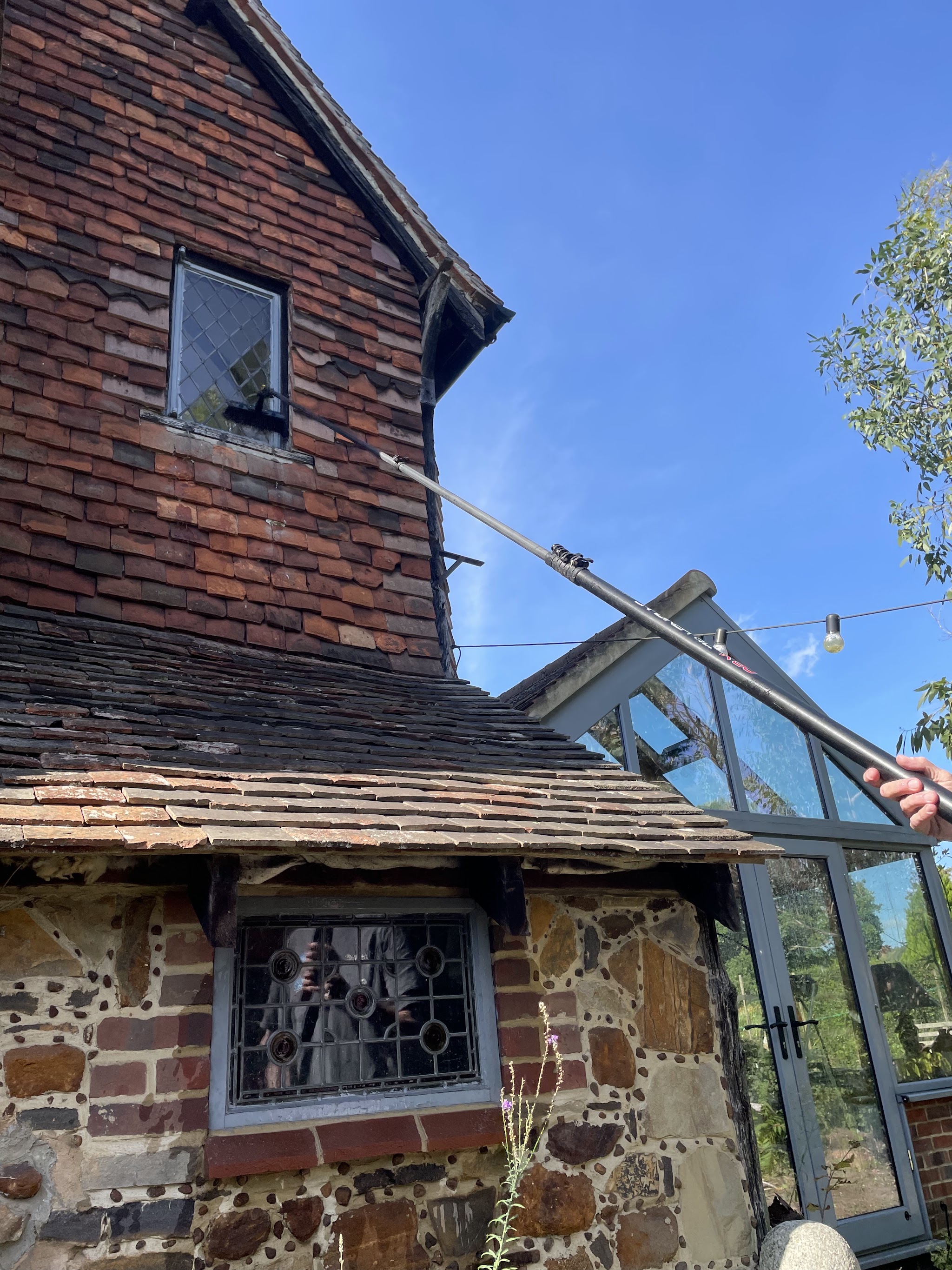 The pole reaching a glass conservatory roof beside an old brick and flint cottage