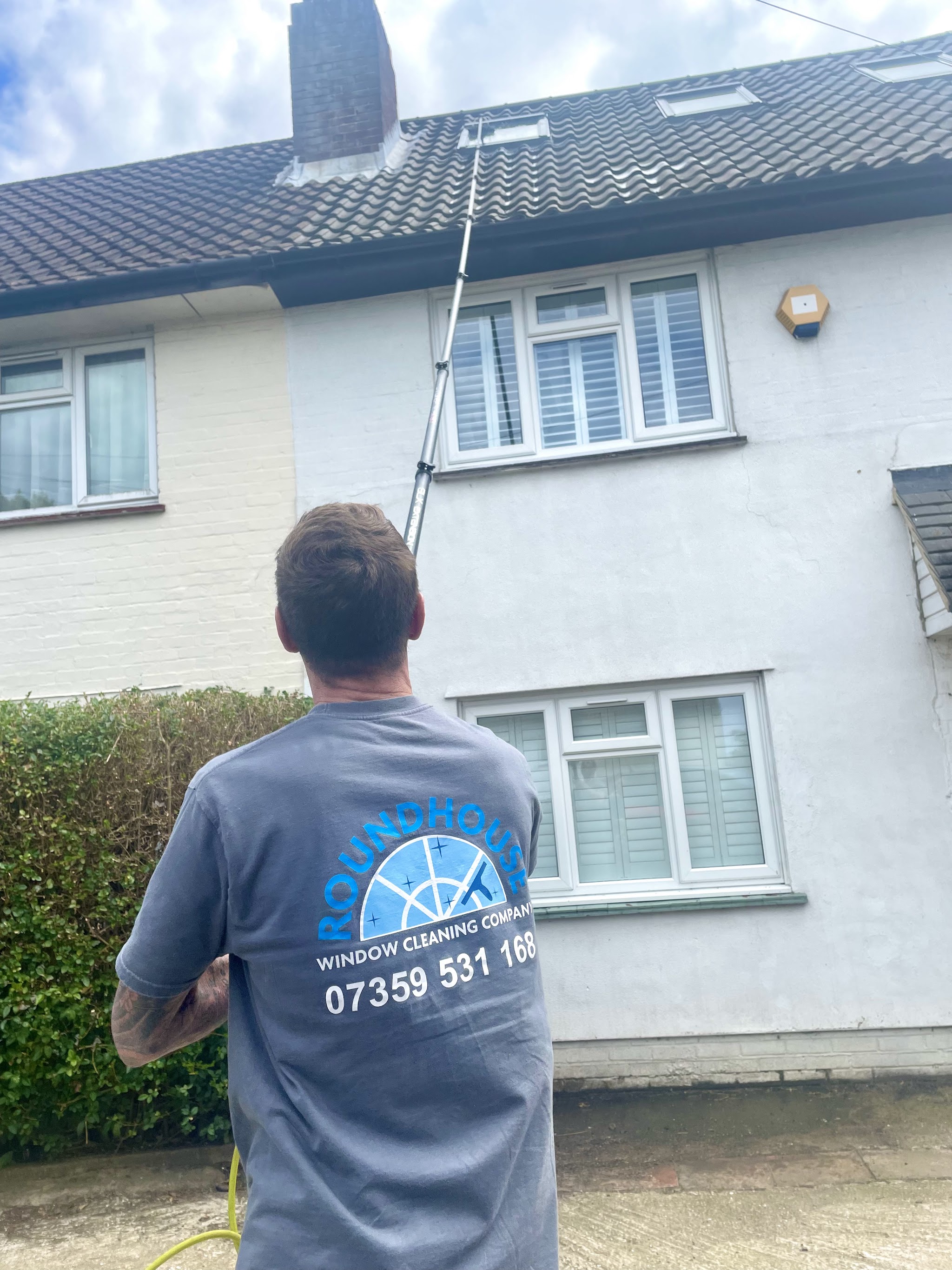 Our window cleaner in a Roundhouse Window Cleaning Company T-shirt, pole up to the first-floor windows of a white house